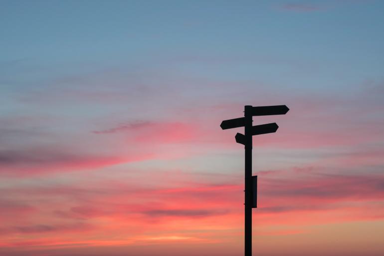 Ein Pfeiler mit Wegweisern, dunkel vor dem Himmel bei Sonnenuntergang