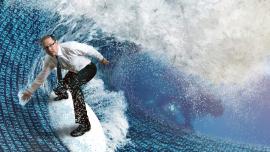Fotomontage: Ein Mann im Businessoutfit steht auf einem Surfbrett und surft auf einer Datenwelle.