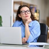 Foto: Insta_Photos - Adobe Stock Eine Frau sitzt nachdenklich an einem Laptop und schaut in die Ferne.